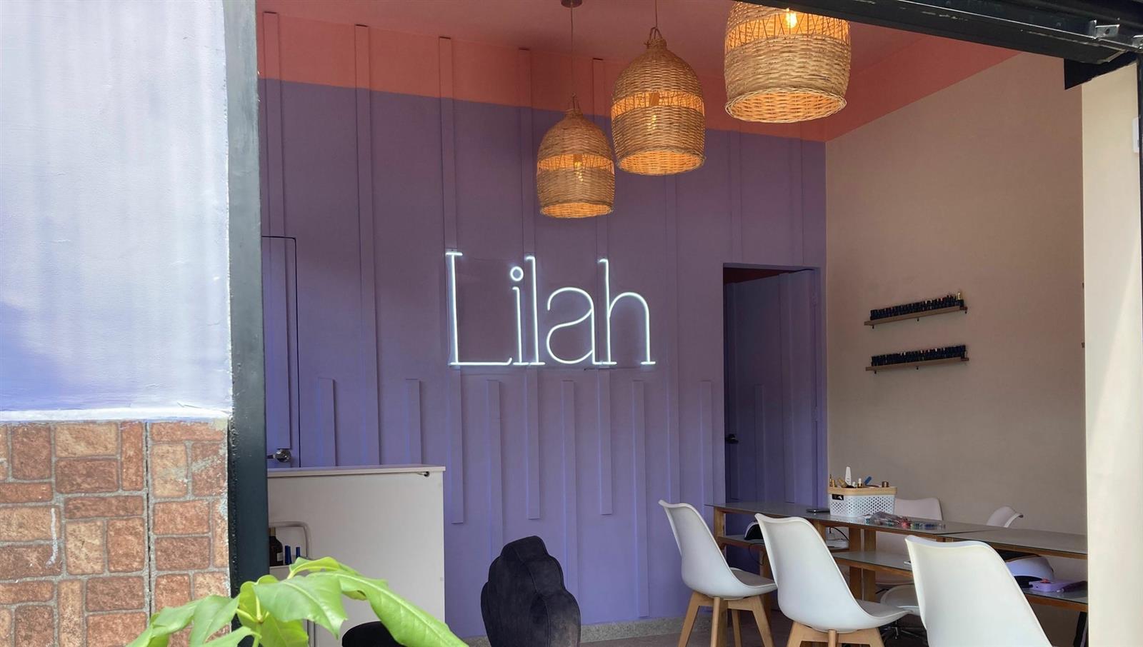 Salón de Lilah con su pared lila, el letrero de neón y lámparas de mimbre